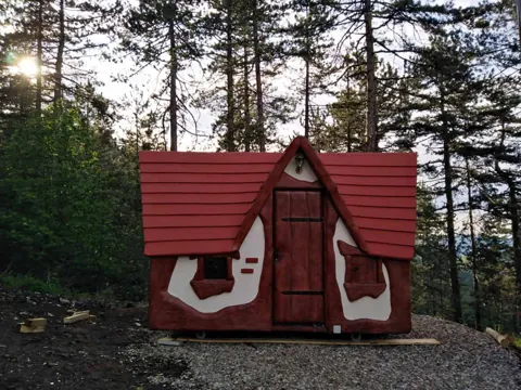 Red roofed cabin tucked between tall forest pines